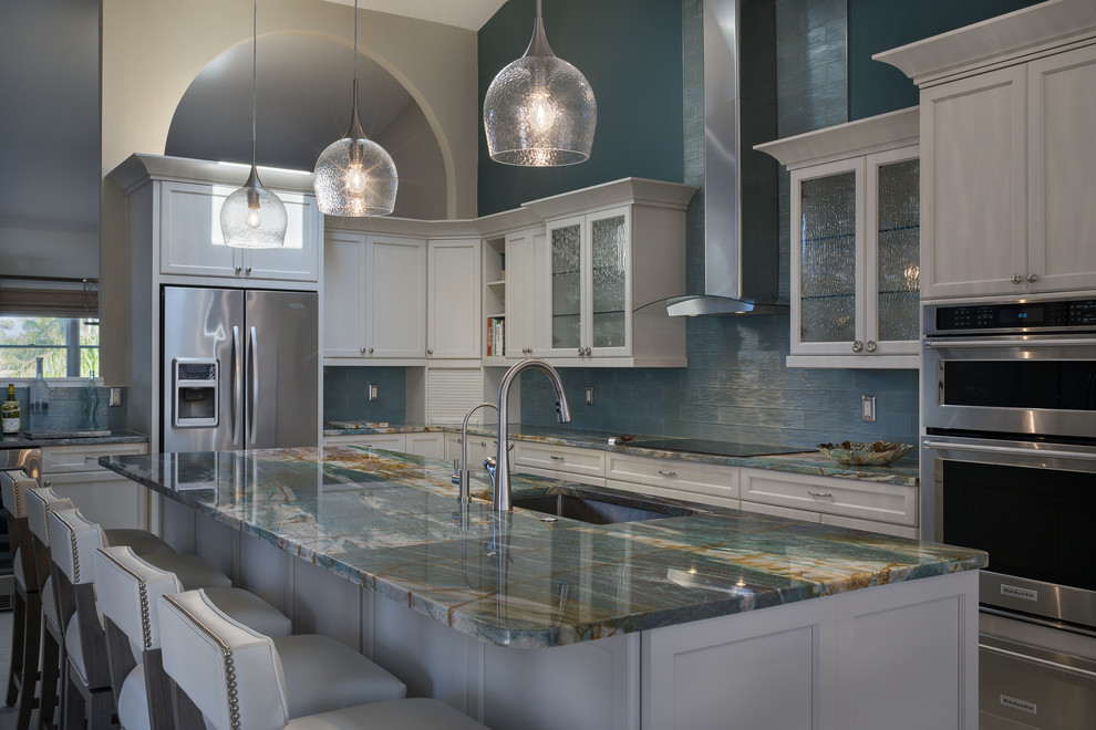 This is an example of a medium sized coastal l-shaped kitchen/diner in Tampa with a submerged sink, recessed-panel cabinets, white cabinets, onyx worktops, blue splashback, glass tiled splashback, stainless steel appliances and an island.