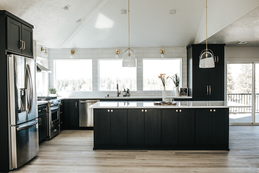 Bild på ett mellanstort funkis vit vitt kök, med en undermonterad diskho, skåp i shakerstil, svarta skåp, bänkskiva i kvartsit, vitt stänkskydd, stänkskydd i keramik, rostfria vitvaror, ljust trägolv, en köksö och grått golv
