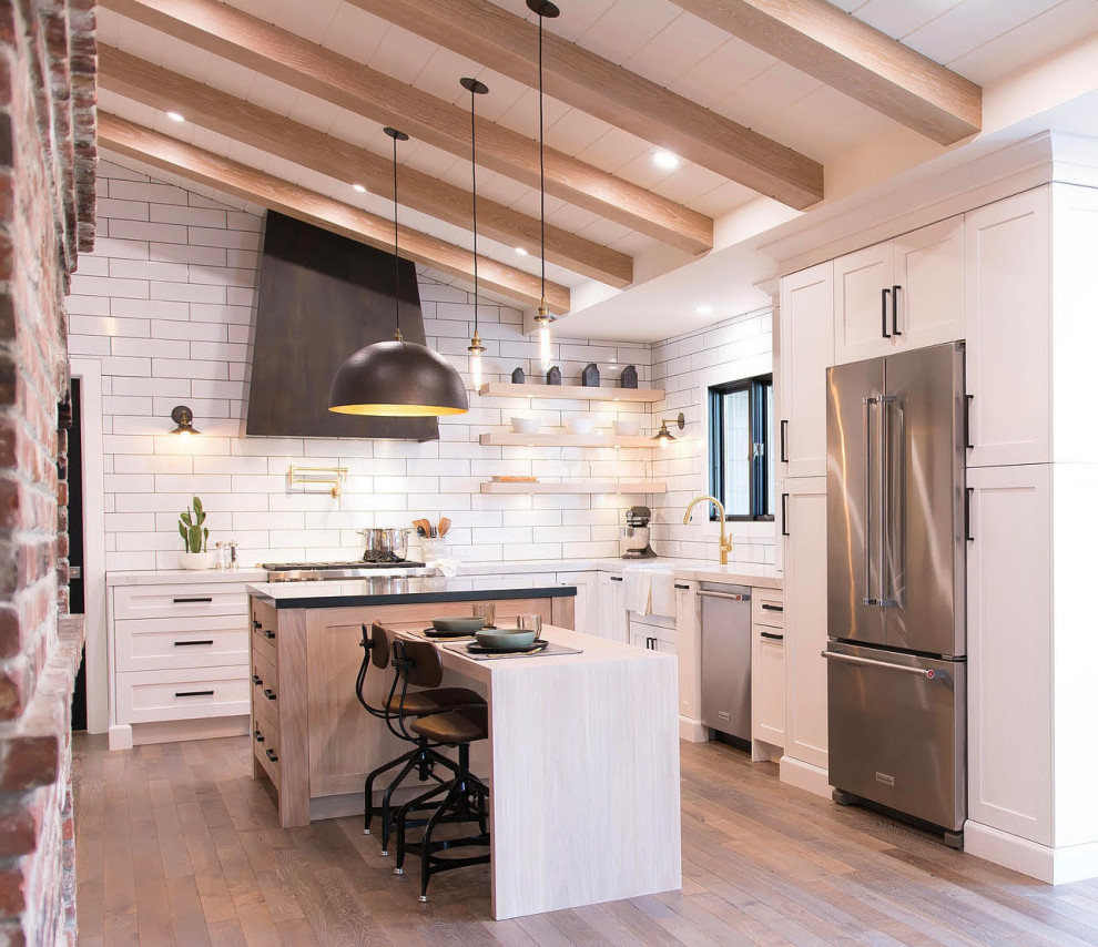 Photo of a rural u-shaped kitchen in San Francisco with a belfast sink, shaker cabinets, white cabinets, white splashback, metro tiled splashback, stainless steel appliances, medium hardwood flooring, an island, brown floors, white worktops, exposed beams, a timber clad ceiling and a vaulted ceiling.