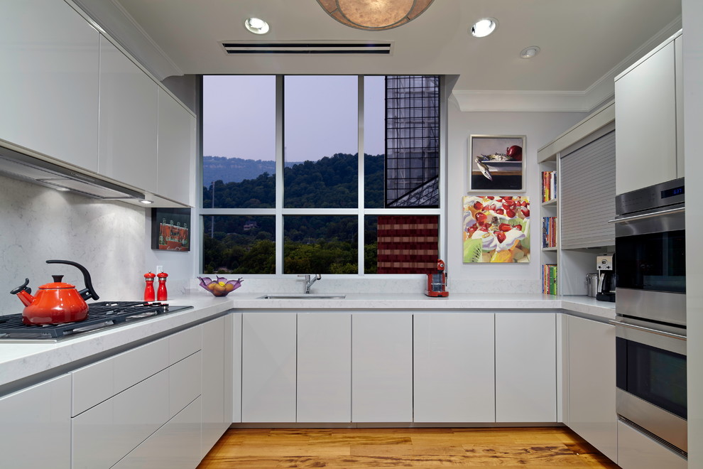 Contemporary u-shaped kitchen/diner in Austin with an integrated sink, white cabinets, white splashback, stone slab splashback and medium hardwood flooring.