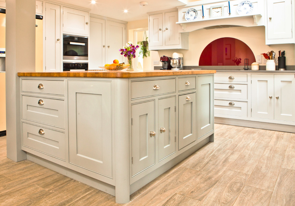 Photo of a large rural u-shaped kitchen/diner in Other with a double-bowl sink, shaker cabinets, grey cabinets, quartz worktops, red splashback, glass sheet splashback, integrated appliances, light hardwood flooring, an island and grey floors.