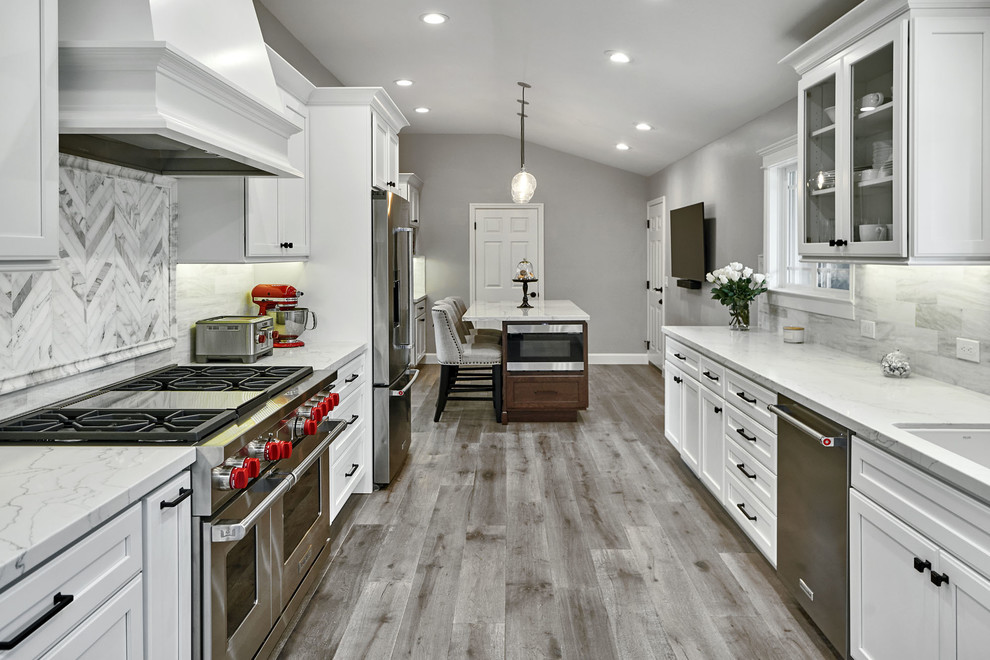 Example of a mid-sized transitional galley light wood floor and gray floor eat-in kitchen design in San Francisco with an undermount sink, flat-panel cabinets, white cabinets, quartz countertops, white backsplash, marble backsplash, stainless steel appliances, an island and white countertops