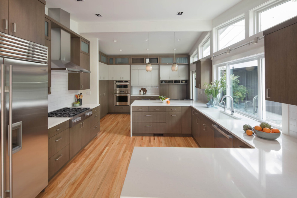 Kitchen - large contemporary u-shaped medium tone wood floor kitchen idea in Seattle with flat-panel cabinets, brown cabinets, quartz countertops, white backsplash, stainless steel appliances, a peninsula and white countertops