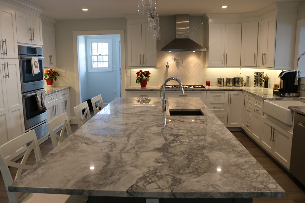 Inspiration for a large transitional porcelain tile and gray floor eat-in kitchen remodel in New York with a farmhouse sink, shaker cabinets, white cabinets, quartzite countertops, white backsplash, ceramic backsplash, stainless steel appliances and an island
