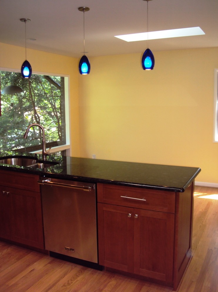Exemple d'une cuisine américaine moderne en U et bois clair de taille moyenne avec un évier encastré, un plan de travail en granite, un électroménager en acier inoxydable et parquet clair.