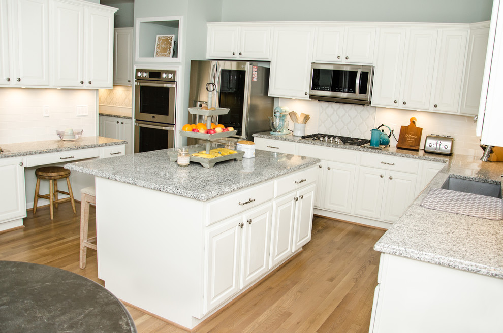 Bild på ett kök, med en undermonterad diskho, vita skåp, bänkskiva i kvarts, vitt stänkskydd, stänkskydd i glaskakel, rostfria vitvaror, ljust trägolv, en köksö och brunt golv