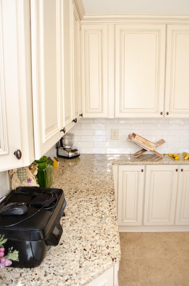 Klassisk inredning av ett beige beige u-kök, med en undermonterad diskho, luckor med infälld panel, vita skåp, granitbänkskiva, vitt stänkskydd, stänkskydd i porslinskakel, rostfria vitvaror, laminatgolv och beiget golv