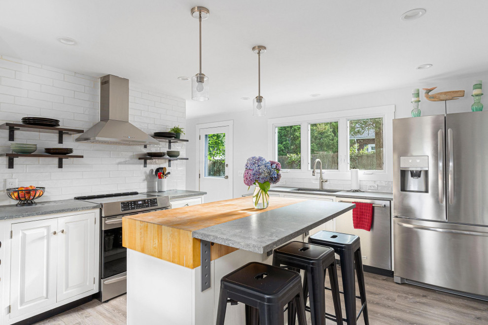 Example of a mid-sized beach style u-shaped light wood floor and gray floor eat-in kitchen design in Providence with a drop-in sink, shaker cabinets, white cabinets, soapstone countertops, white backsplash, subway tile backsplash, stainless steel appliances, an island and gray countertops