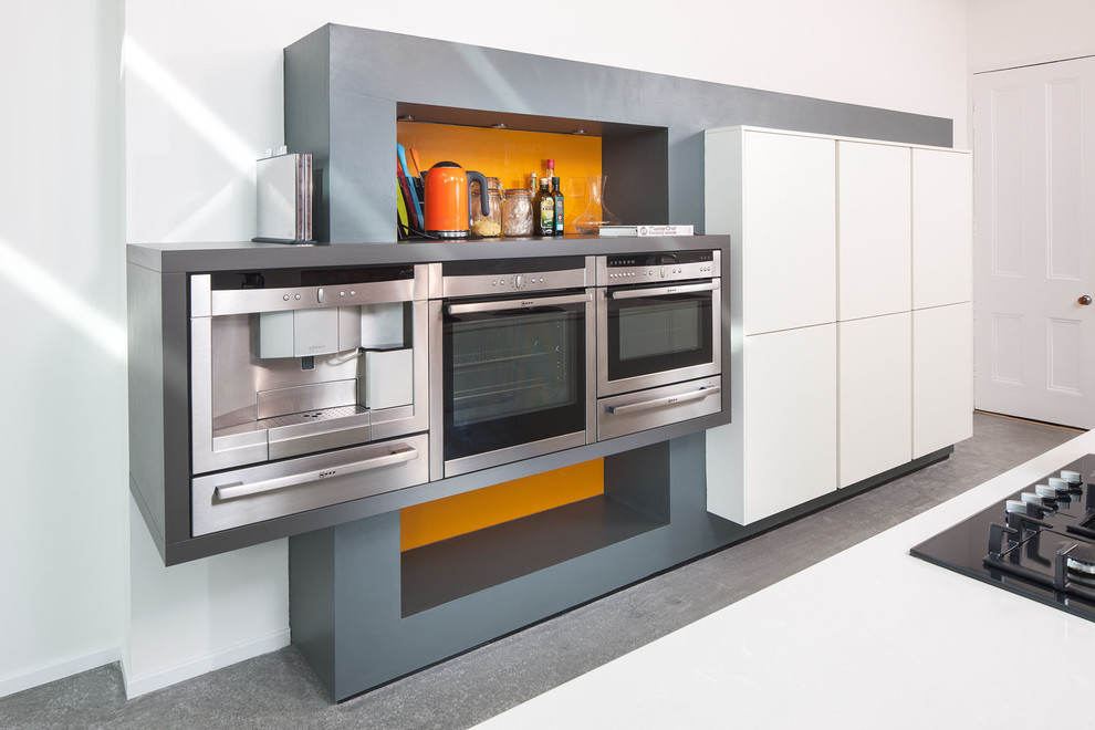 Esempio di una grande cucina moderna con lavello a vasca singola, ante lisce, ante bianche, paraspruzzi arancione, elettrodomestici in acciaio inossidabile e pavimento in cemento