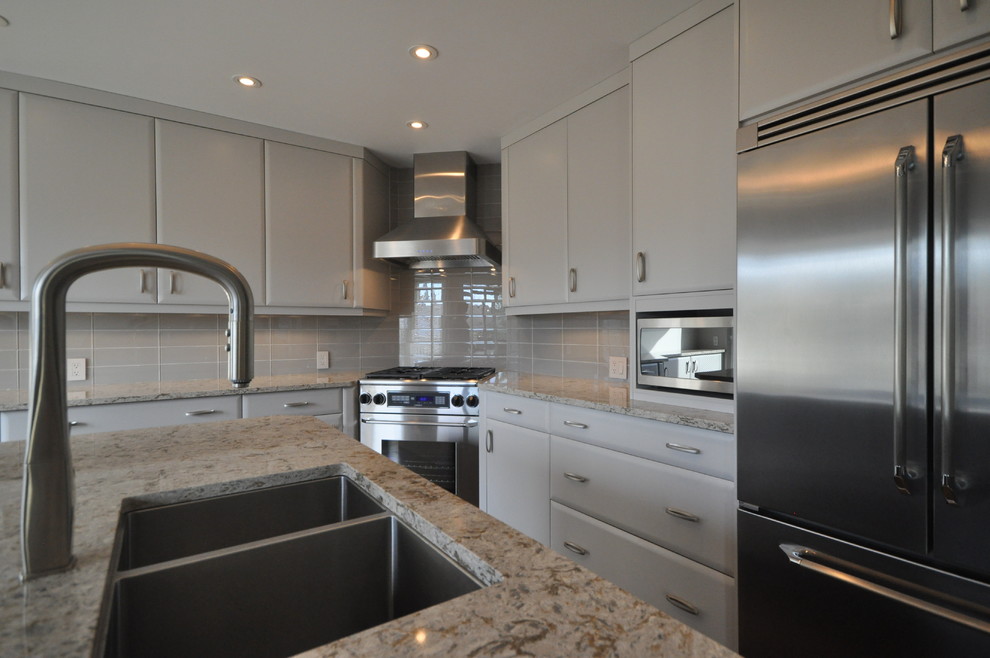 Photo of a medium sized contemporary l-shaped kitchen/diner in Toronto with a submerged sink, raised-panel cabinets, grey cabinets, engineered stone countertops, grey splashback, glass tiled splashback, stainless steel appliances, medium hardwood flooring and an island.
