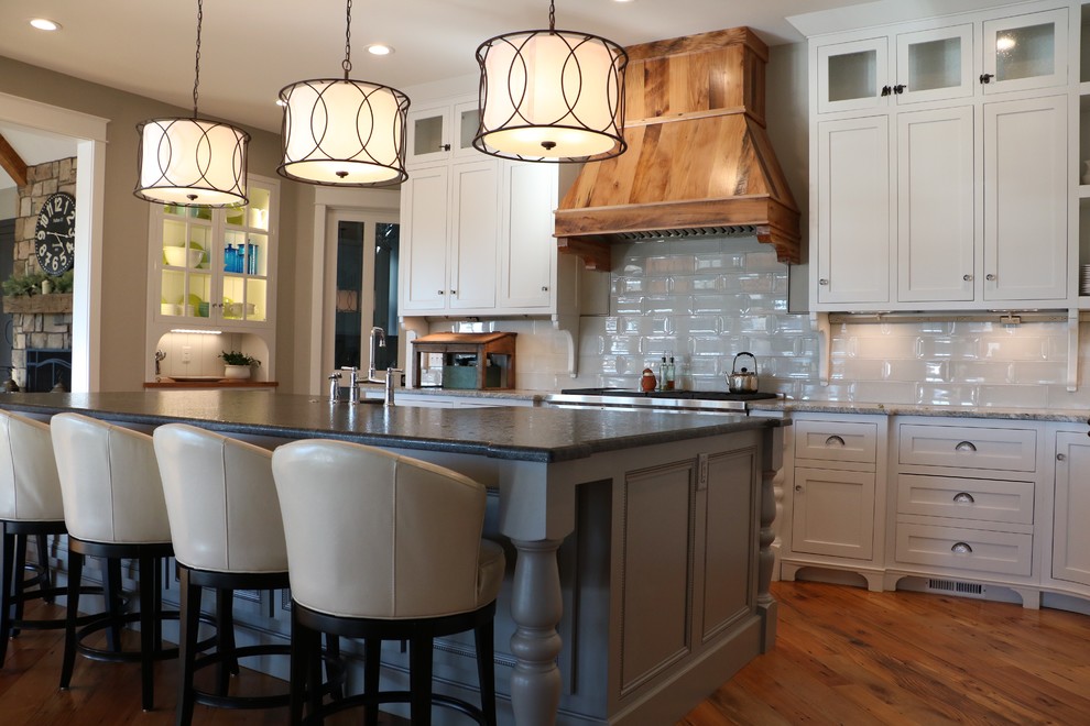 Open concept kitchen - large country medium tone wood floor open concept kitchen idea in Other with a farmhouse sink, shaker cabinets, white cabinets, granite countertops, gray backsplash, porcelain backsplash, stainless steel appliances, an island and gray countertops