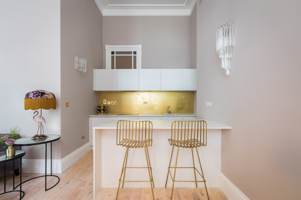 This is an example of a medium sized contemporary single-wall kitchen in London with a submerged sink, flat-panel cabinets, white cabinets, metallic splashback, light hardwood flooring, beige floors and white worktops.