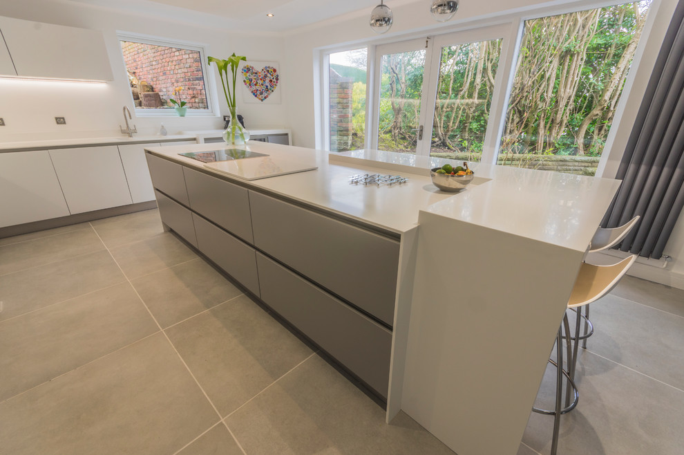 Modern kitchen in Cheshire with flat-panel cabinets, white cabinets, white splashback, cement flooring and an island.
