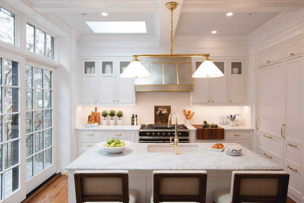 Klassisk inredning av ett grå grått l-kök, med en undermonterad diskho, luckor med infälld panel, vita skåp, brunt stänkskydd, svarta vitvaror, mellanmörkt trägolv, en köksö och brunt golv