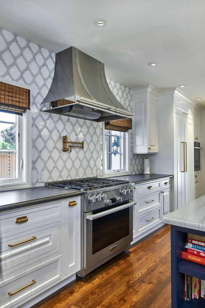 Example of a large transitional l-shaped medium tone wood floor and brown floor kitchen pantry design in San Francisco with a farmhouse sink, beaded inset cabinets, white cabinets, granite countertops, gray backsplash, mosaic tile backsplash, paneled appliances, an island and black countertops