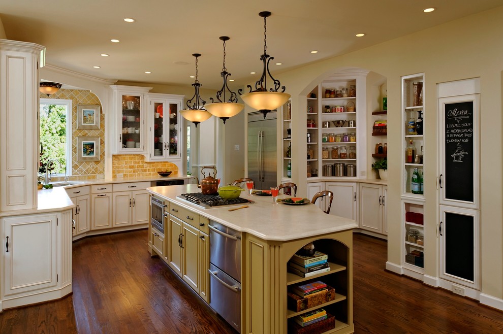 Example of a large french country l-shaped dark wood floor open concept kitchen design in DC Metro with stone tile backsplash, stainless steel appliances, an undermount sink, white cabinets, solid surface countertops, beige backsplash, an island and recessed-panel cabinets