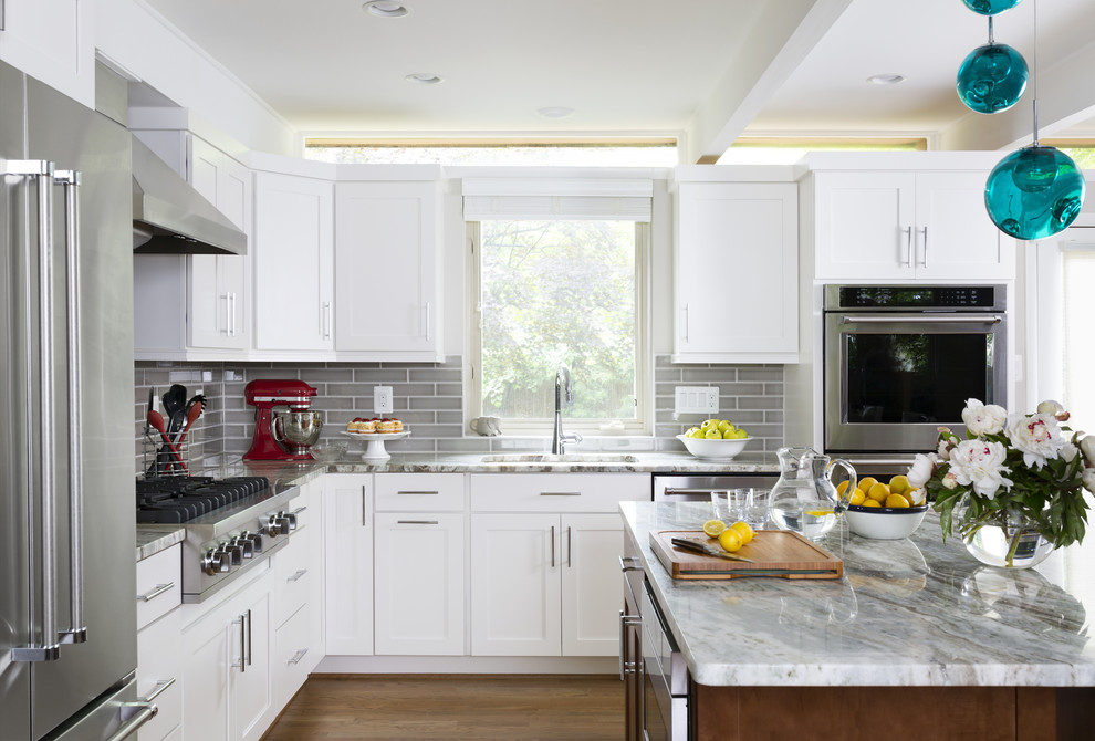 Inspiration for a large transitional l-shaped brown floor and medium tone wood floor kitchen remodel in DC Metro with an undermount sink, shaker cabinets, white cabinets, marble countertops, gray backsplash, ceramic backsplash, stainless steel appliances and an island