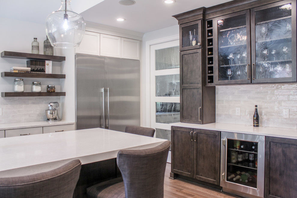 Large transitional l-shaped medium tone wood floor and brown floor eat-in kitchen photo in Detroit with a farmhouse sink, shaker cabinets, white cabinets, quartz countertops, white backsplash, porcelain backsplash, stainless steel appliances, an island and white countertops