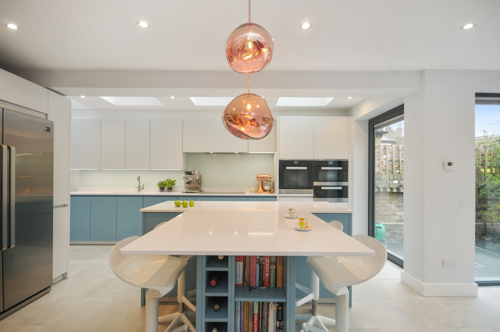 Inspiration for a large contemporary kitchen in London with flat-panel cabinets, blue cabinets, green splashback, stainless steel appliances, an island, beige floors, white worktops and glass sheet splashback.