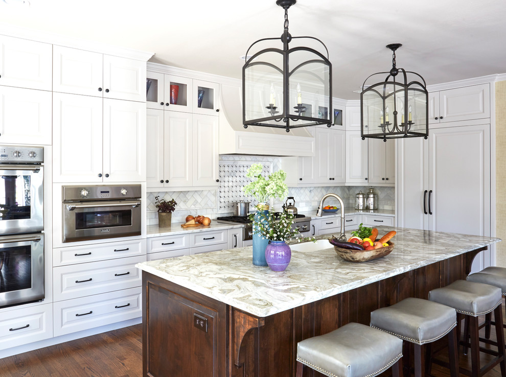 Exempel på ett klassiskt l-kök, med en undermonterad diskho, luckor med upphöjd panel, vita skåp, vitt stänkskydd, stänkskydd i marmor, integrerade vitvaror, mörkt trägolv, en köksö och brunt golv