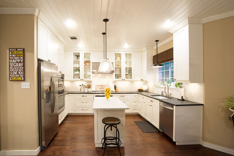 Inspiration for a transitional u-shaped medium tone wood floor eat-in kitchen remodel in Austin with an undermount sink, shaker cabinets, white cabinets, white backsplash, ceramic backsplash, stainless steel appliances and an island