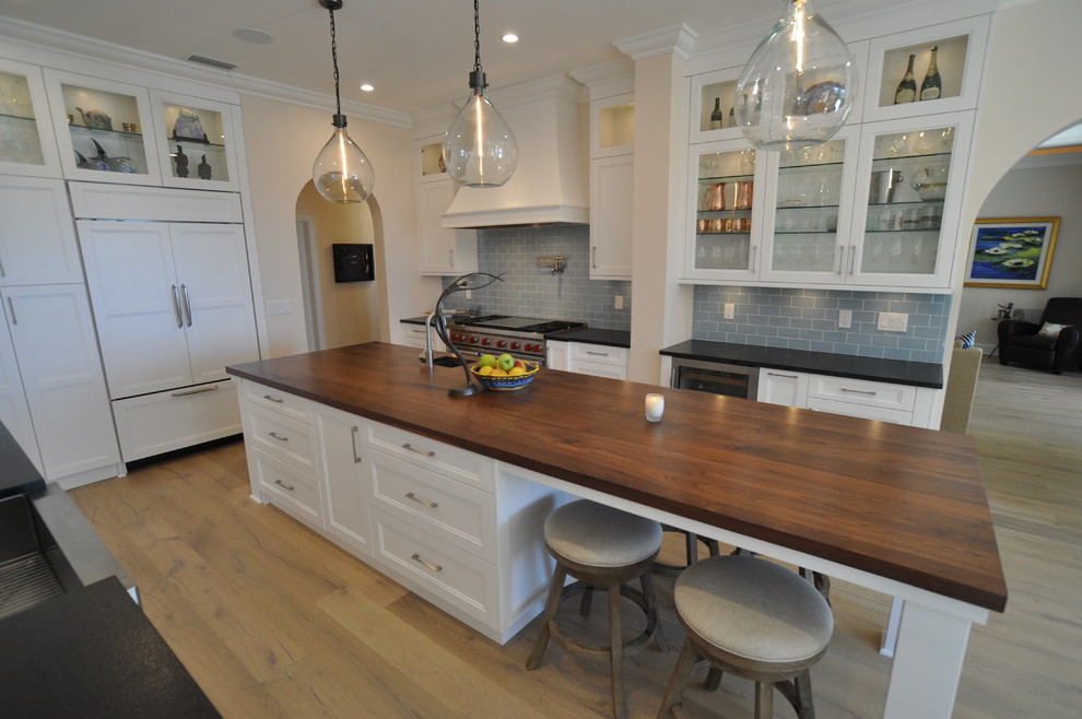 Inspiration for a large transitional galley medium tone wood floor eat-in kitchen remodel in Tampa with a farmhouse sink, shaker cabinets, white cabinets, granite countertops, blue backsplash, subway tile backsplash, stainless steel appliances and an island