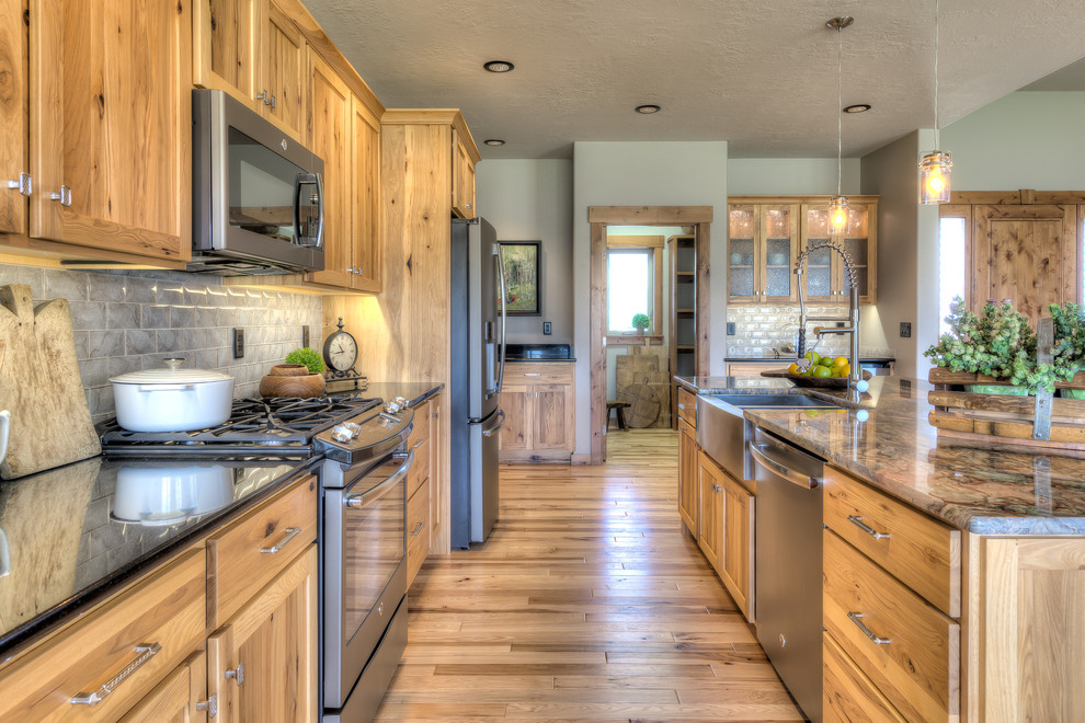 Example of a mountain style galley light wood floor and beige floor kitchen design in Other with shaker cabinets, medium tone wood cabinets, gray backsplash, subway tile backsplash, an island and a farmhouse sink