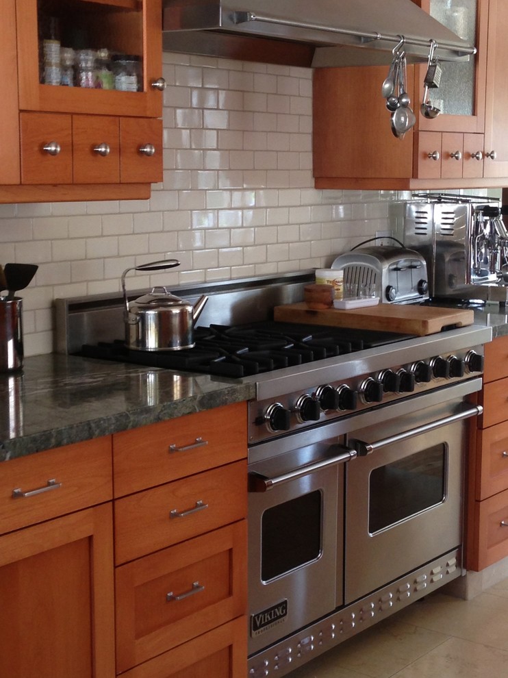 Bild på ett avskilt, mellanstort amerikanskt u-kök, med en nedsänkt diskho, skåp i shakerstil, skåp i mellenmörkt trä, granitbänkskiva, vitt stänkskydd, stänkskydd i keramik, rostfria vitvaror och travertin golv