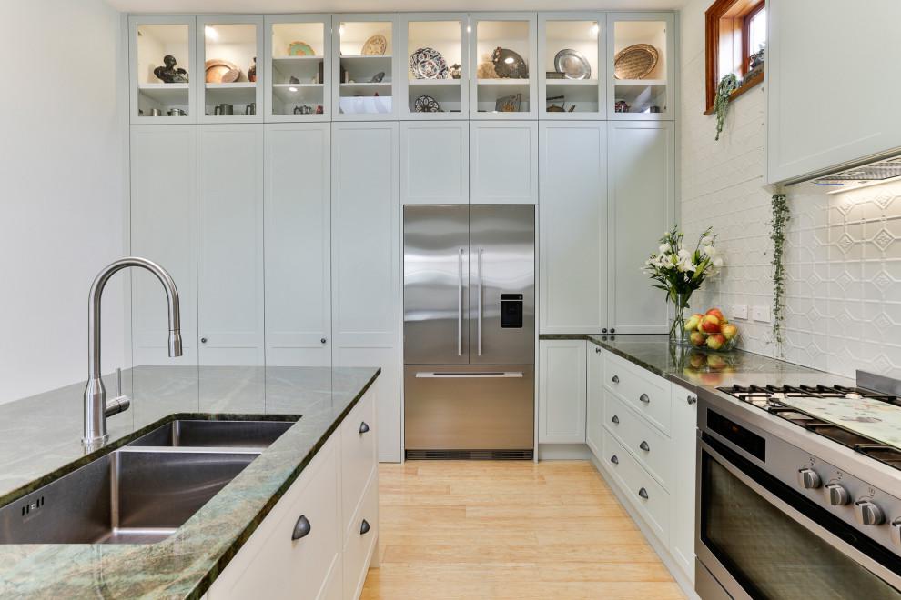Example of a large classic l-shaped bamboo floor kitchen pantry design in Christchurch with an undermount sink, shaker cabinets, green cabinets, granite countertops, green backsplash, metal backsplash, stainless steel appliances, an island and green countertops