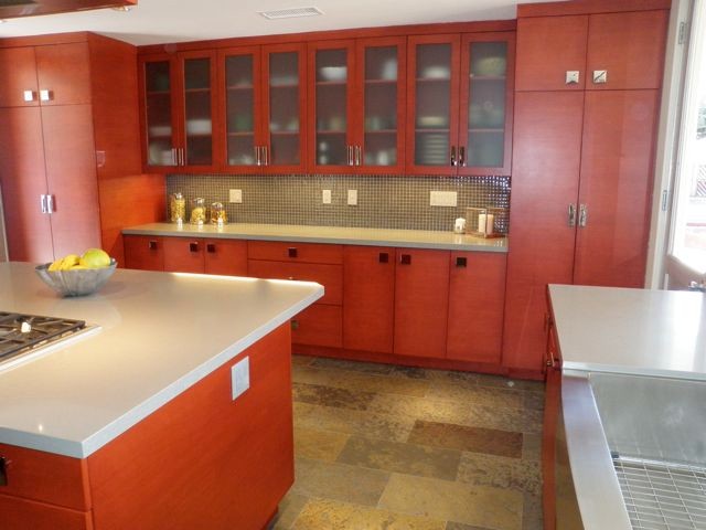 This is an example of a large modern u-shaped enclosed kitchen in Los Angeles with a belfast sink, flat-panel cabinets, red cabinets, engineered stone countertops, grey splashback, glass tiled splashback, stainless steel appliances, slate flooring, an island, multi-coloured floors and grey worktops.