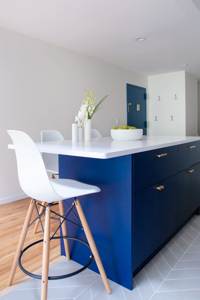 This is an example of a medium sized modern single-wall open plan kitchen in New York with a submerged sink, flat-panel cabinets, blue cabinets, engineered stone countertops, blue splashback, cement tile splashback, stainless steel appliances, porcelain flooring, an island, grey floors and white worktops.