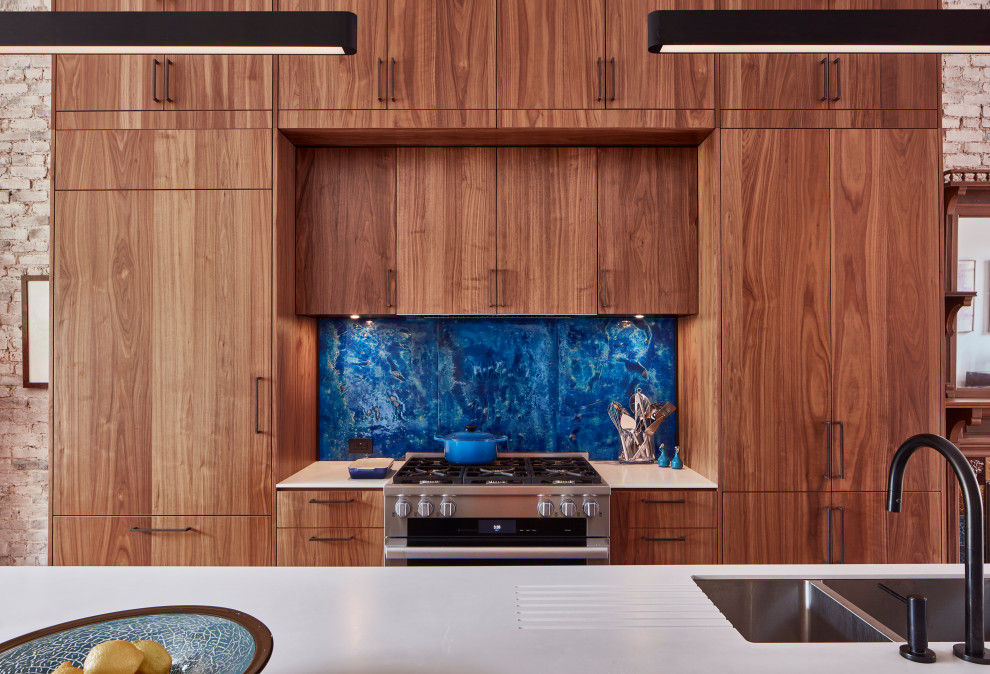 Klassische Wohnküche mit Doppelwaschbecken, flächenbündigen Schrankfronten, hellbraunen Holzschränken, Küchenrückwand in Blau, Elektrogeräten mit Frontblende, hellem Holzboden, Kücheninsel und weißer Arbeitsplatte in New York