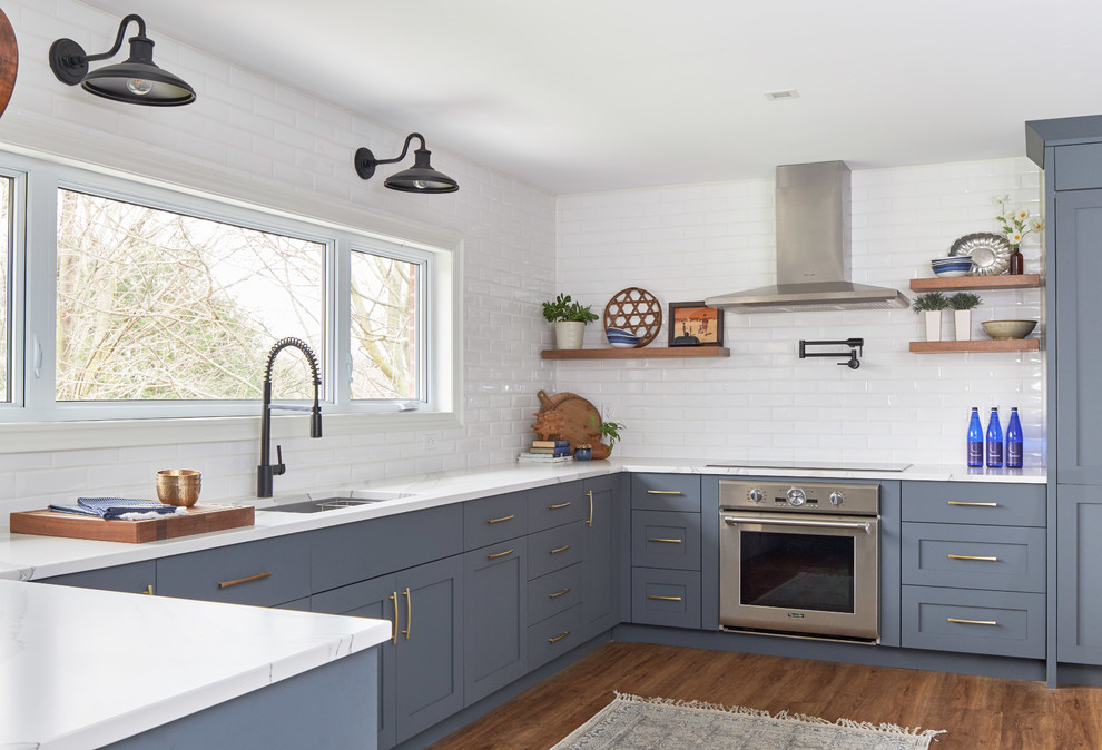 This is an example of a large country u-shaped kitchen/diner in Toronto with a double-bowl sink, shaker cabinets, blue cabinets, laminate countertops, white splashback, ceramic splashback, stainless steel appliances, dark hardwood flooring, a breakfast bar, brown floors and white worktops.