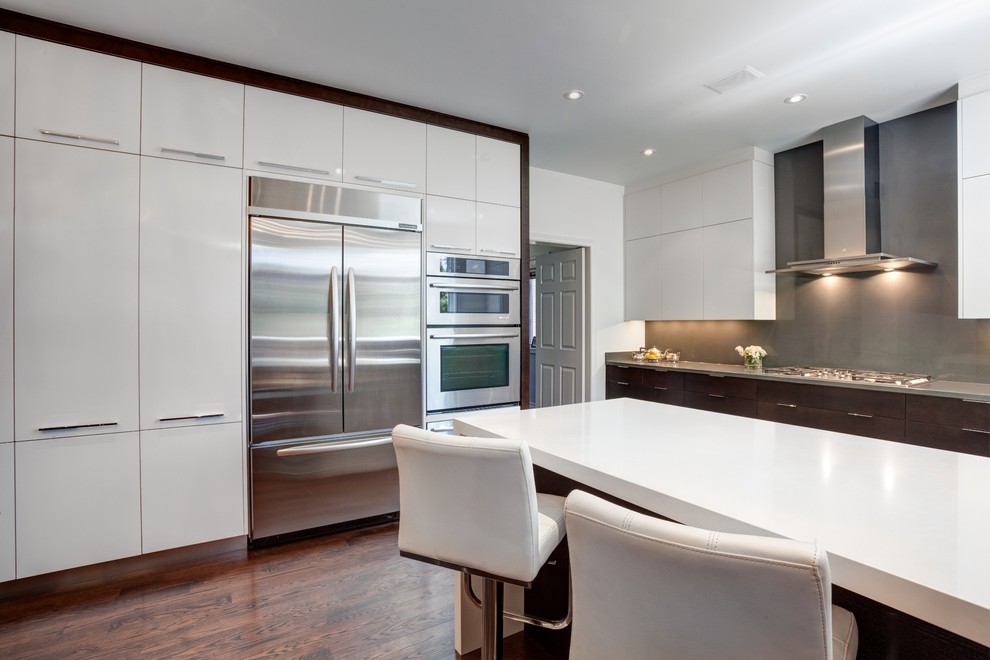 This is an example of a large contemporary u-shaped kitchen/diner in Toronto with flat-panel cabinets, white cabinets, engineered stone countertops, grey splashback, stone slab splashback, stainless steel appliances, dark hardwood flooring and a breakfast bar.