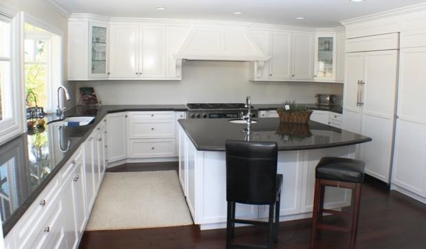 This is an example of a large traditional u-shaped enclosed kitchen in Orange County with a submerged sink, shaker cabinets, white cabinets, engineered stone countertops, white splashback, integrated appliances, dark hardwood flooring, an island, brown floors and black worktops.