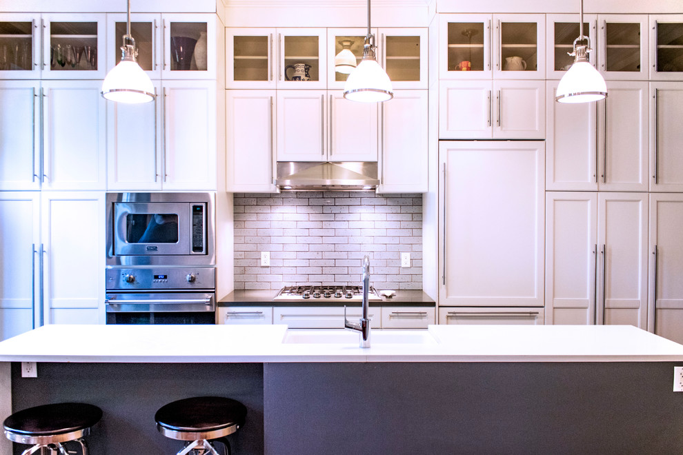お手頃価格の中くらいなトランジショナルスタイルのおしゃれなキッチン (エプロンフロントシンク、シェーカースタイル扉のキャビネット、白いキャビネット、クオーツストーンカウンター、青いキッチンパネル、磁器タイルのキッチンパネル、シルバーの調理設備、無垢フローリング、茶色い床、白いキッチンカウンター) の写真