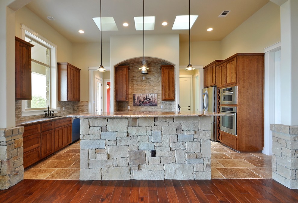 Inspiration for a large southwestern u-shaped travertine floor kitchen remodel in Austin with an undermount sink, recessed-panel cabinets, medium tone wood cabinets, granite countertops, brown backsplash, stone tile backsplash, stainless steel appliances and an island
