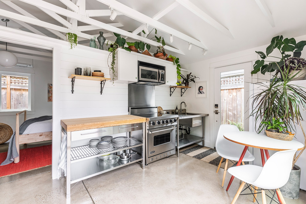 Foto på ett litet maritimt linjärt kök och matrum, med en enkel diskho, träbänkskiva, vitt stänkskydd, stänkskydd i trä, rostfria vitvaror, betonggolv och grått golv