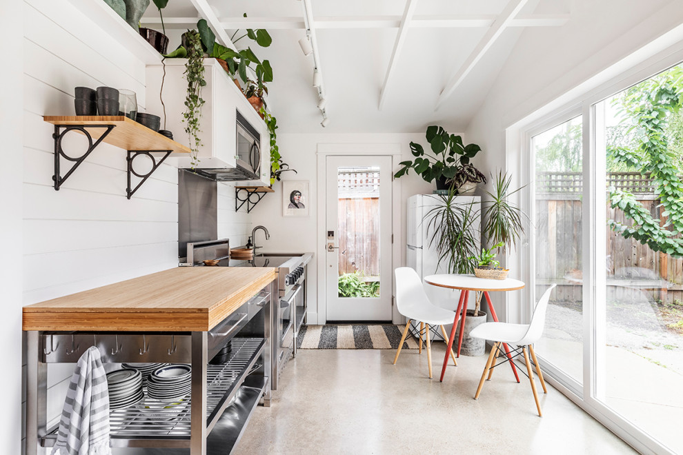 Immagine di una piccola cucina costiera con top in legno, paraspruzzi bianco, paraspruzzi in legno, pavimento in cemento, elettrodomestici in acciaio inossidabile e pavimento grigio