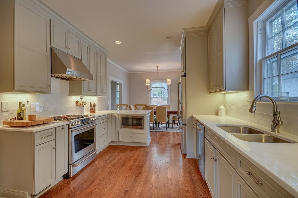 Eat-in kitchen - mid-sized traditional galley medium tone wood floor eat-in kitchen idea in Birmingham with an undermount sink, recessed-panel cabinets, gray cabinets, quartzite countertops, white backsplash, subway tile backsplash, stainless steel appliances and a peninsula