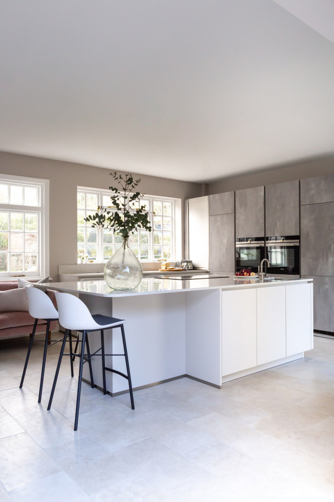 Große Moderne Küche in L-Form mit integriertem Waschbecken, flächenbündigen Schrankfronten, grauen Schränken, Quarzit-Arbeitsplatte, Küchenrückwand in Weiß, Rückwand aus Quarzwerkstein, Keramikboden, Kücheninsel, grauem Boden und weißer Arbeitsplatte in Oxfordshire