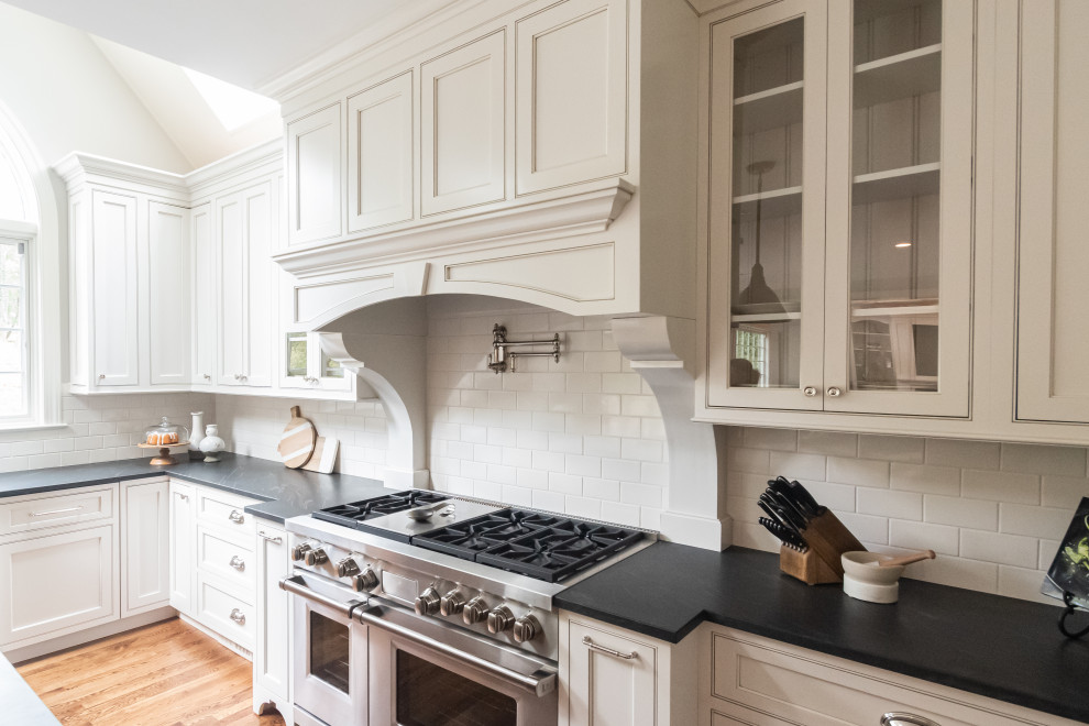 Inspiration for a large timeless u-shaped medium tone wood floor and brown floor open concept kitchen remodel in Philadelphia with a farmhouse sink, beaded inset cabinets, white cabinets, granite countertops, white backsplash, subway tile backsplash, paneled appliances, an island and black countertops
