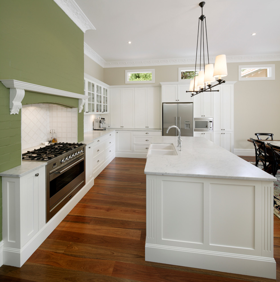 Klassisk inredning av ett stort vit vitt kök, med skåp i shakerstil, vita skåp, marmorbänkskiva, vitt stänkskydd, stänkskydd i keramik, rostfria vitvaror, en köksö, en rustik diskho, mellanmörkt trägolv och brunt golv