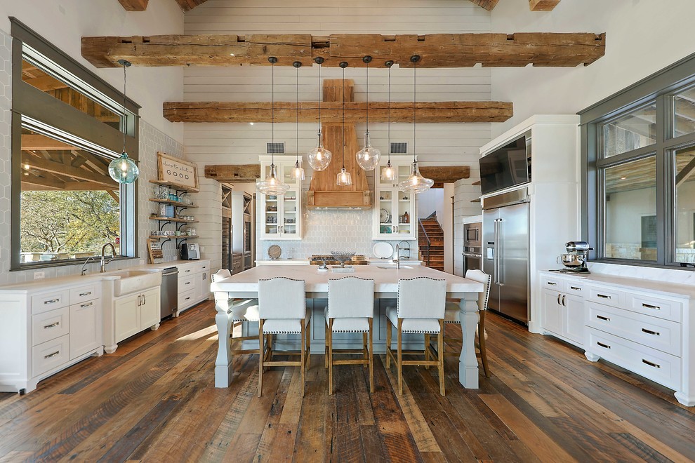 Bild på ett mycket stort lantligt vit vitt kök, med vita skåp, en köksö, en rustik diskho, skåp i shakerstil, vitt stänkskydd, rostfria vitvaror, mellanmörkt trägolv och brunt golv