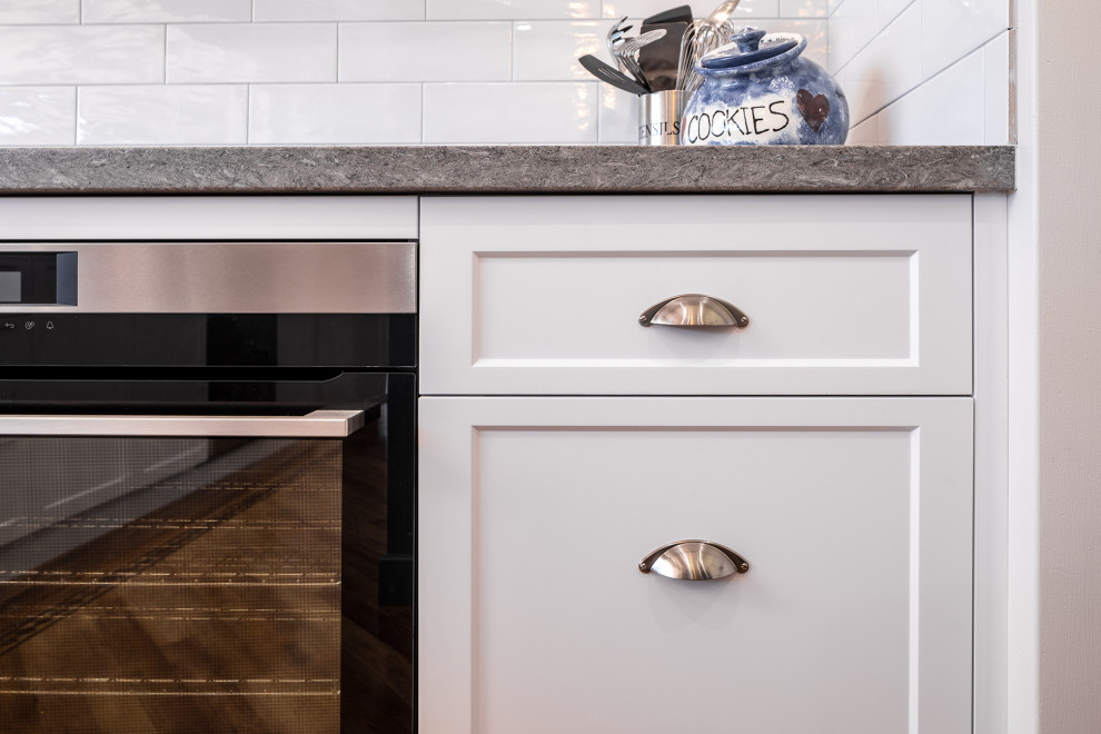 Modern inredning av ett grå grått kök, med skåp i shakerstil, vita skåp, bänkskiva i kvarts, vitt stänkskydd, stänkskydd i tunnelbanekakel, mellanmörkt trägolv och en köksö