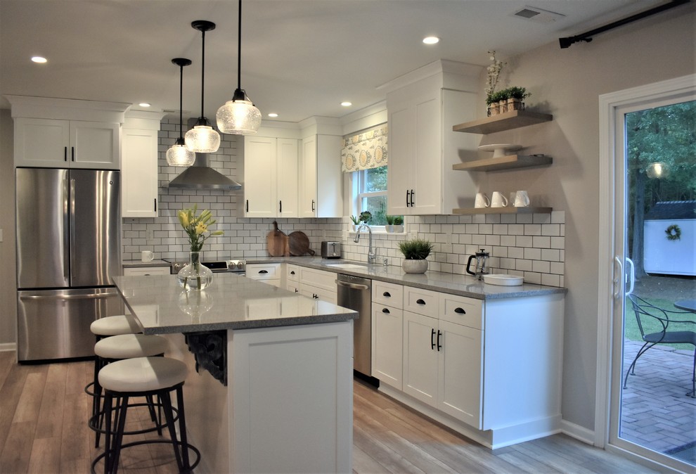 Idéer för ett mellanstort klassiskt grå kök, med skåp i shakerstil, vita skåp, en köksö, en undermonterad diskho, granitbänkskiva, vitt stänkskydd, stänkskydd i tunnelbanekakel, rostfria vitvaror, laminatgolv och brunt golv