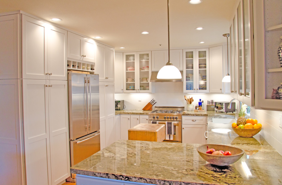 Cette photo montre une cuisine moderne en U fermée avec un placard à porte vitrée, des portes de placard blanches, une crédence blanche et un électroménager en acier inoxydable.