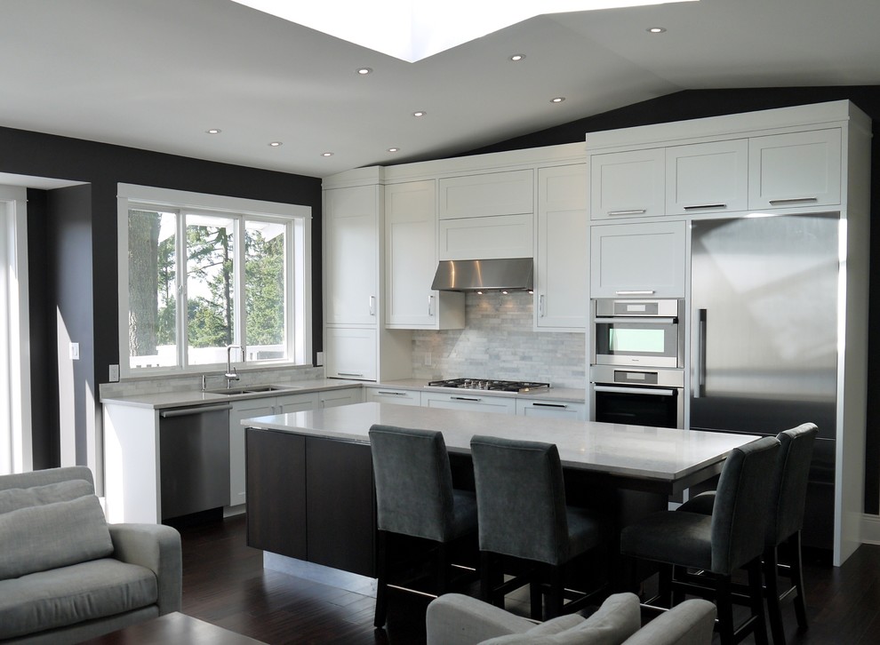 This is an example of a medium sized contemporary l-shaped open plan kitchen in Vancouver with a submerged sink, shaker cabinets, white cabinets, engineered stone countertops, grey splashback, stone tiled splashback, stainless steel appliances, dark hardwood flooring and an island.