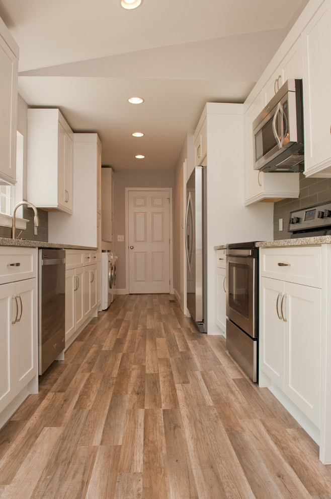 Example of a mid-sized trendy galley medium tone wood floor enclosed kitchen design in Charlotte with an undermount sink, raised-panel cabinets, white cabinets, granite countertops, gray backsplash, glass tile backsplash, stainless steel appliances and no island