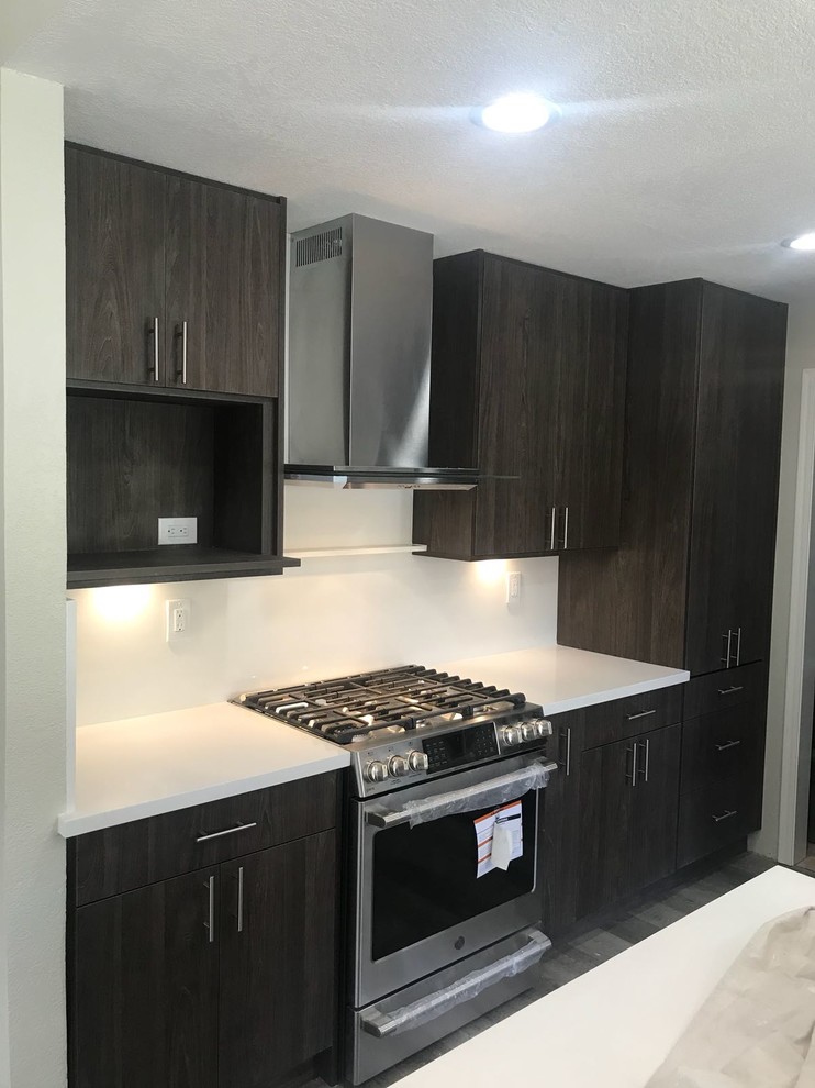Modelo de cocinas en L actual, de tamaño medio, abierta, con fregadero bajoencimera, armarios con paneles lisos, puertas de armario de madera en tonos medios, encimera de cuarzo compacto, salpicadero blanco, electrodomésticos de acero inoxidable, suelo de madera oscura, una isla, suelo marrón, encimeras blancas y salpicadero de vidrio templado